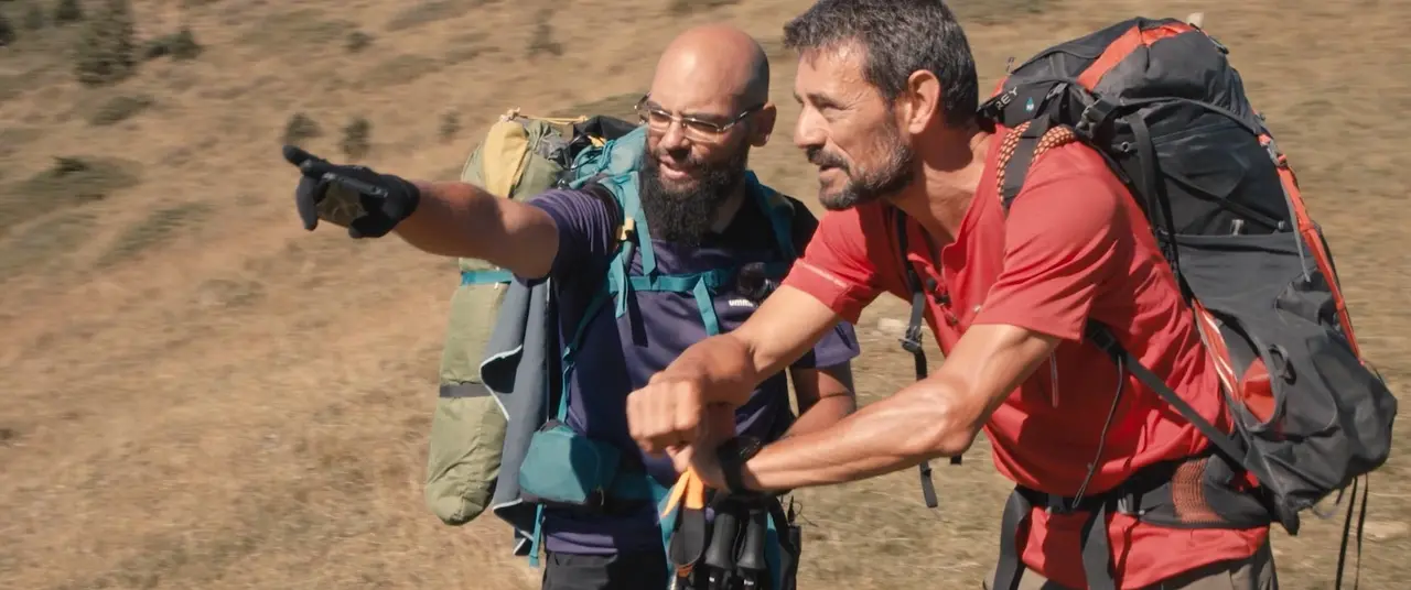 Deux marcheurs en montagne, l’un désigne un point au loin, bâtons de randonnée à la main.