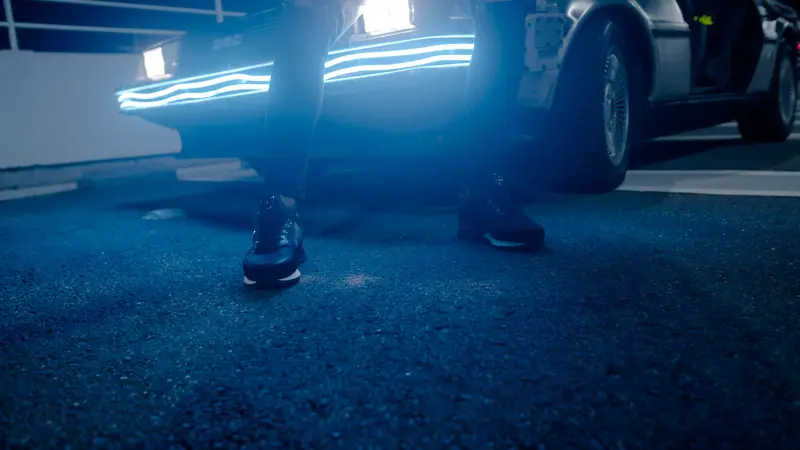 Des baskets noires sur l’asphalte, devant une voiture éclairée de néons bleus.